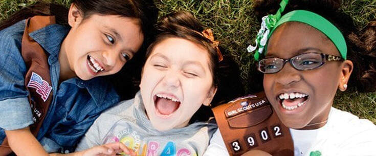 Closeup of three Girl Scouts laughing on a lawn